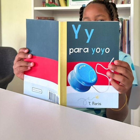 Child holding a book titled 'Y y para yoyo' by T. Paris in a home setting.